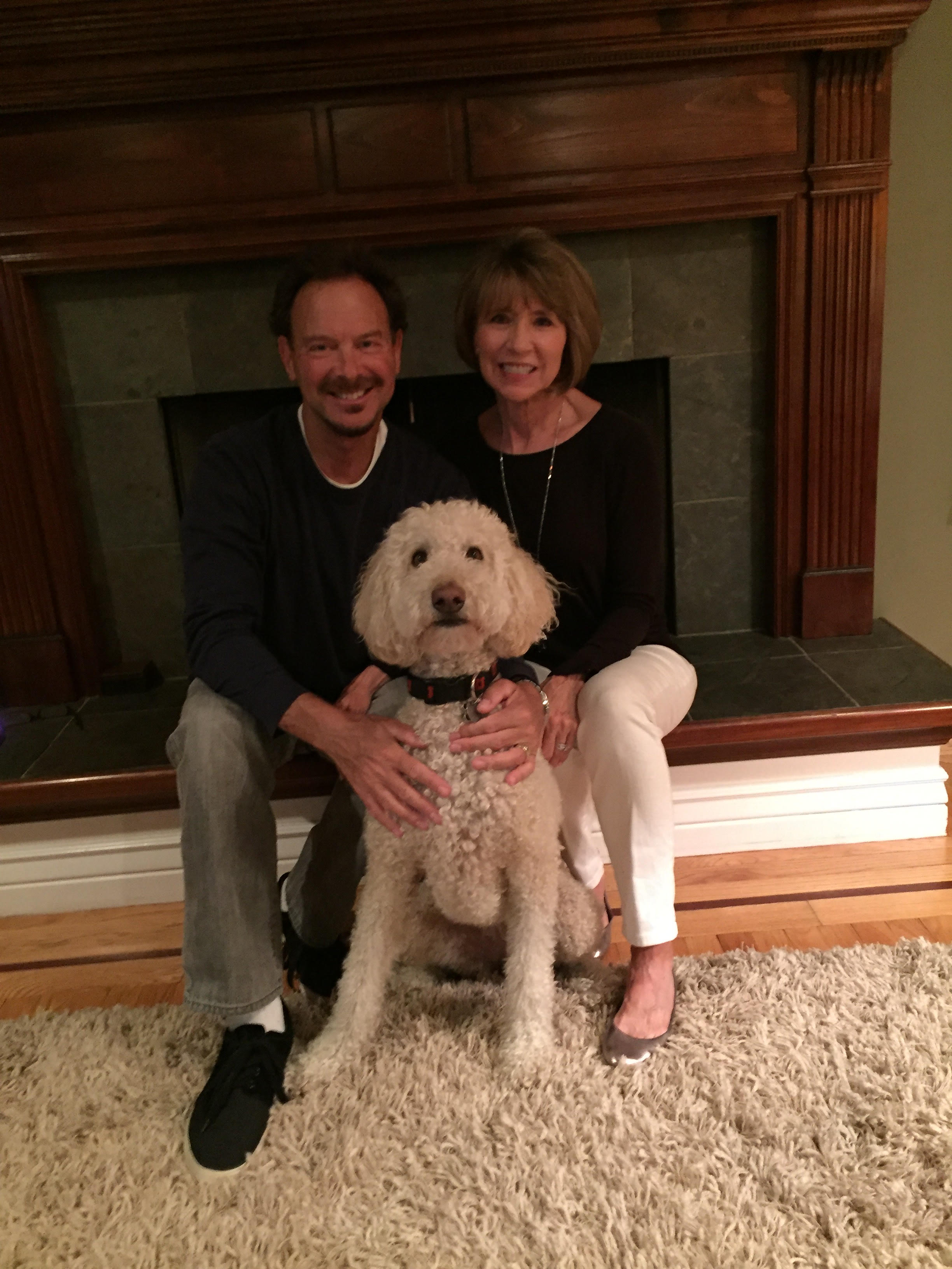 Paul, Wendy and their dog taking a family photo infront of a fireplace